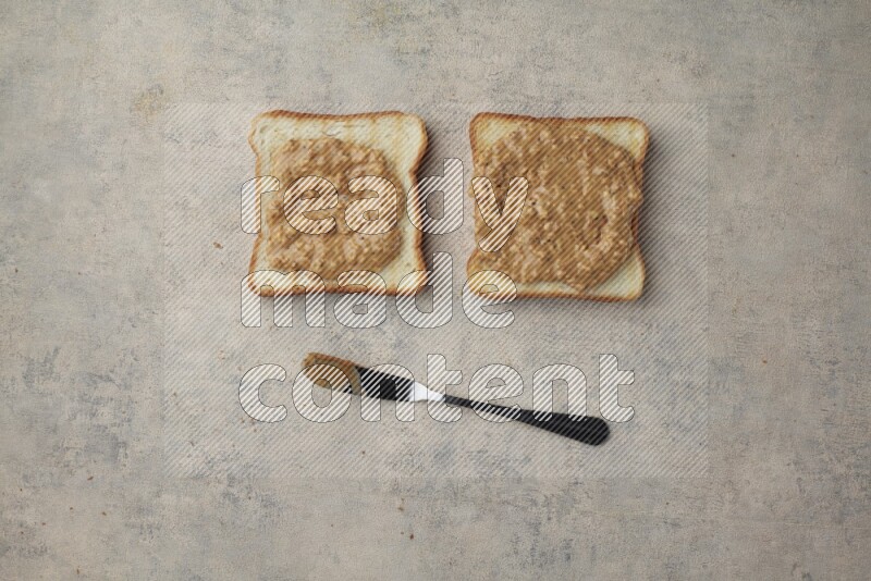 Crunchy  peanut butter on a toasted white toast slices with a spreading knife on a light blue textured background