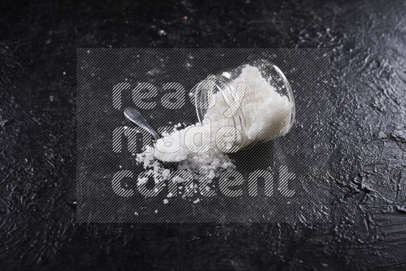 A glass jar full of coarse sea salt crystals on black background