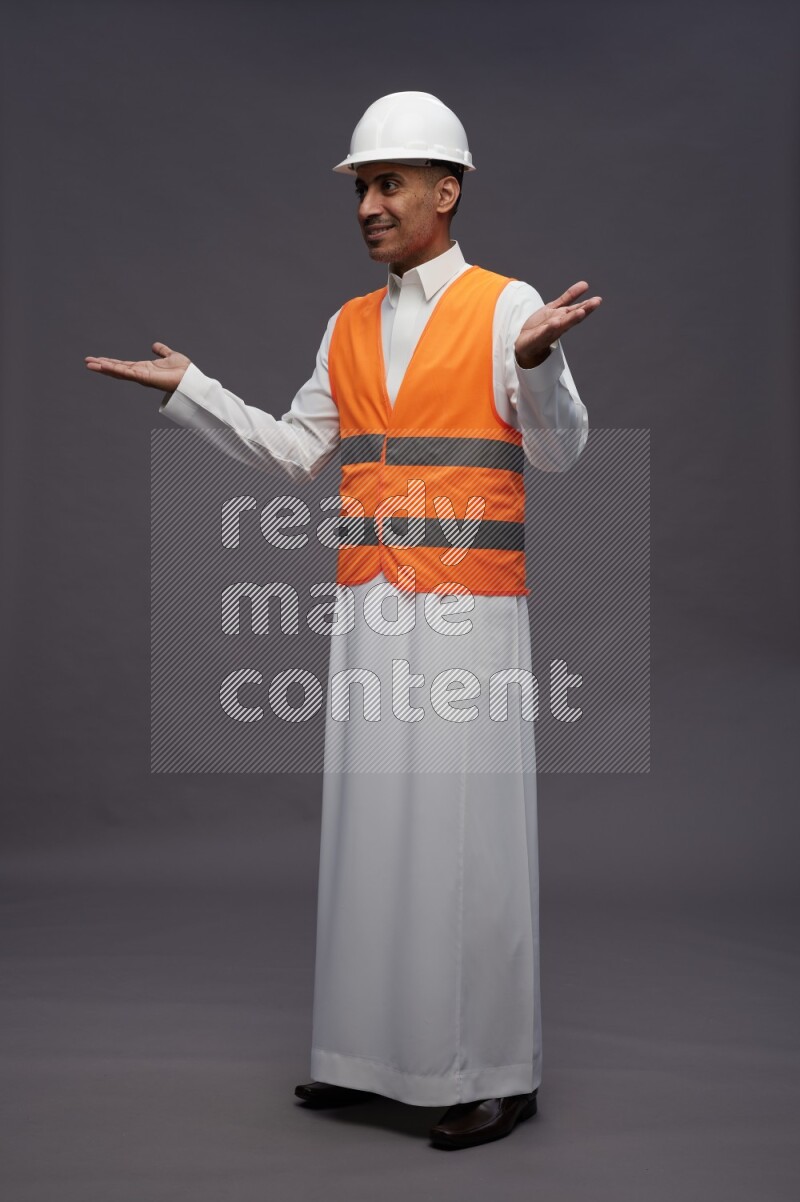Saudi man wearing thob with engineer vest standing interacting with the camera on gray background