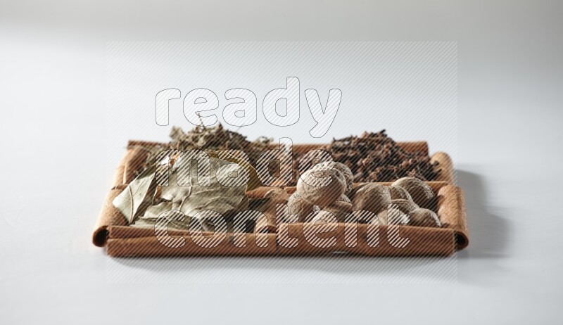 4 مربعات من أعواد القرفة ممتلئة بأوراق الغار والريحان المجفف والقرنفل وجوزة الطيب على أرضية بيضاء