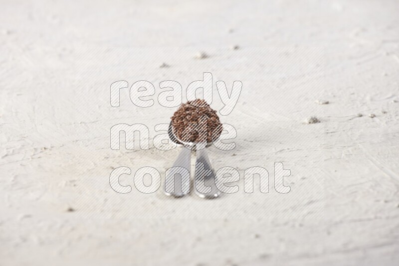 2 metal spoons full of flax seeds on a textured white flooring