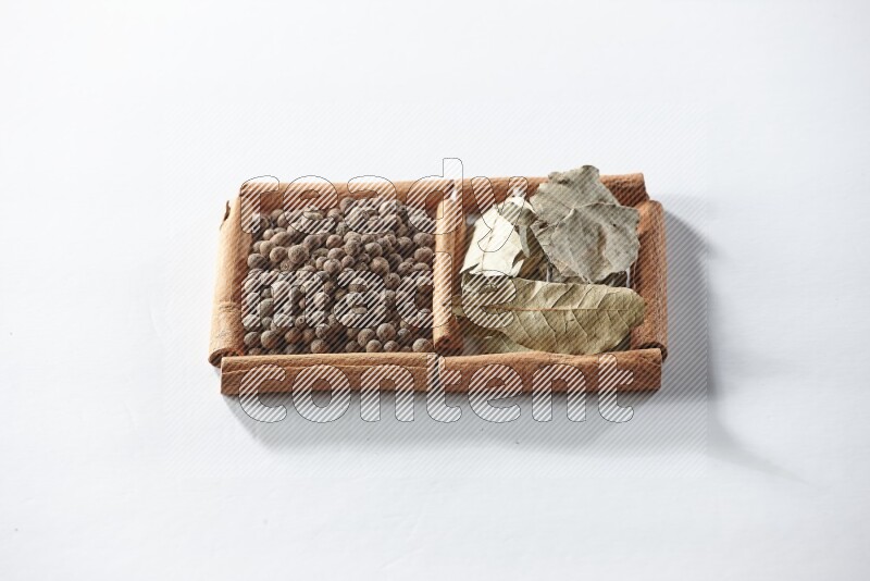 مربعان من أعواد القرفة ممتلئان ببهار الفلفل الحلو وأوراق الغار علي خلفية بيضاء