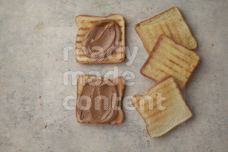 Creamy peanut butter on a toasted white toast and toasted white toast slices on a light blue textured background