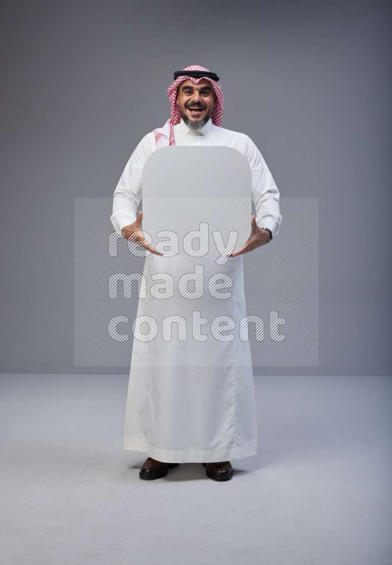 Saudi man Wearing Thob and red Shomag standing holding social media sign on Gray background