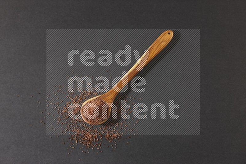 A wooden ladle full of garden cress seeds and seeds spread beside it on a black flooring