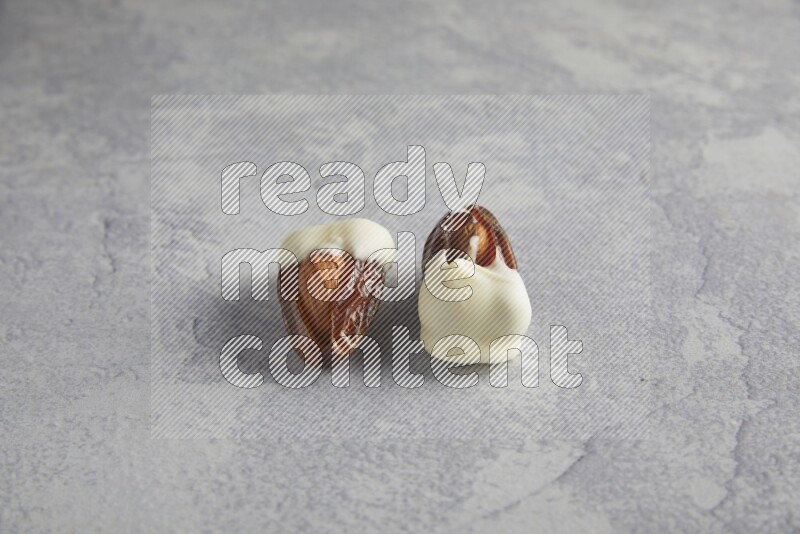 two almonds stuffed dates covered with white chololate on a light grey background