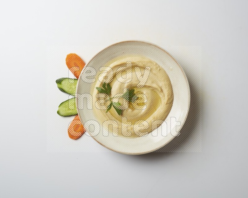 Hummus in a pottry plate garnished with parsley on a white back ground