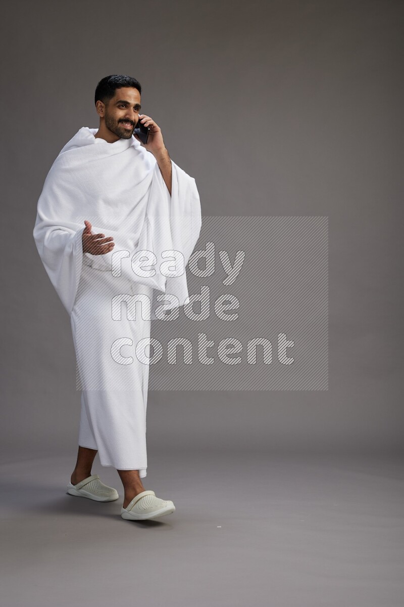 A man wearing Ehram Standing talking on phone on gray background