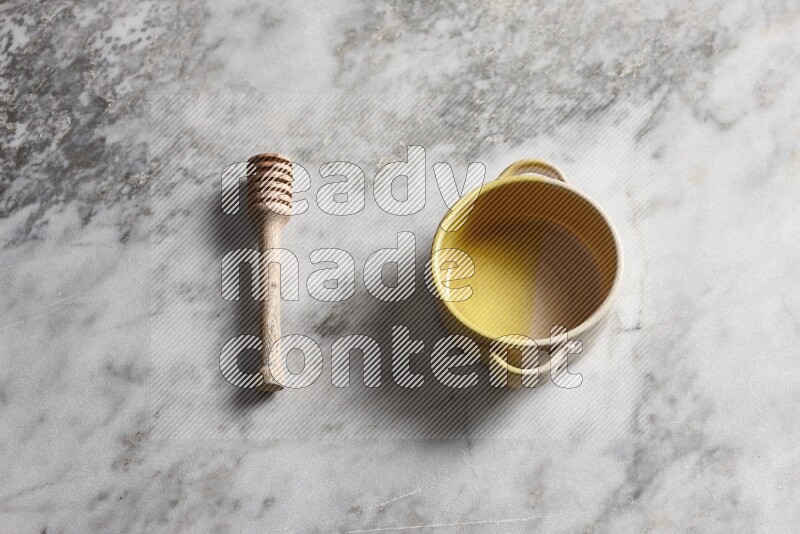 Multicolored pottery bowl with wooden honey dipper on the side on grey marble background