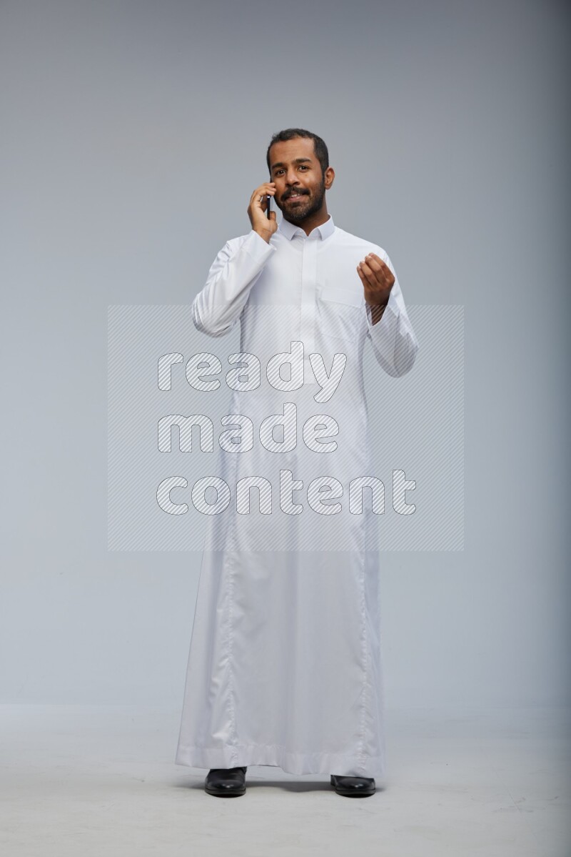 Saudi man wearing Thob standing talking on phone on Gray background