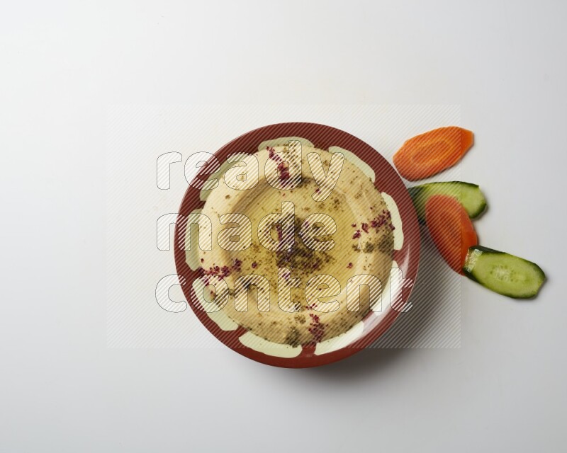 Hummus in a traditional plate garnished with zaatar & sumak on a white background