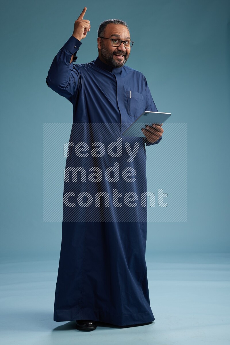 Saudi Man without shimag Standing working on tablet on blue background