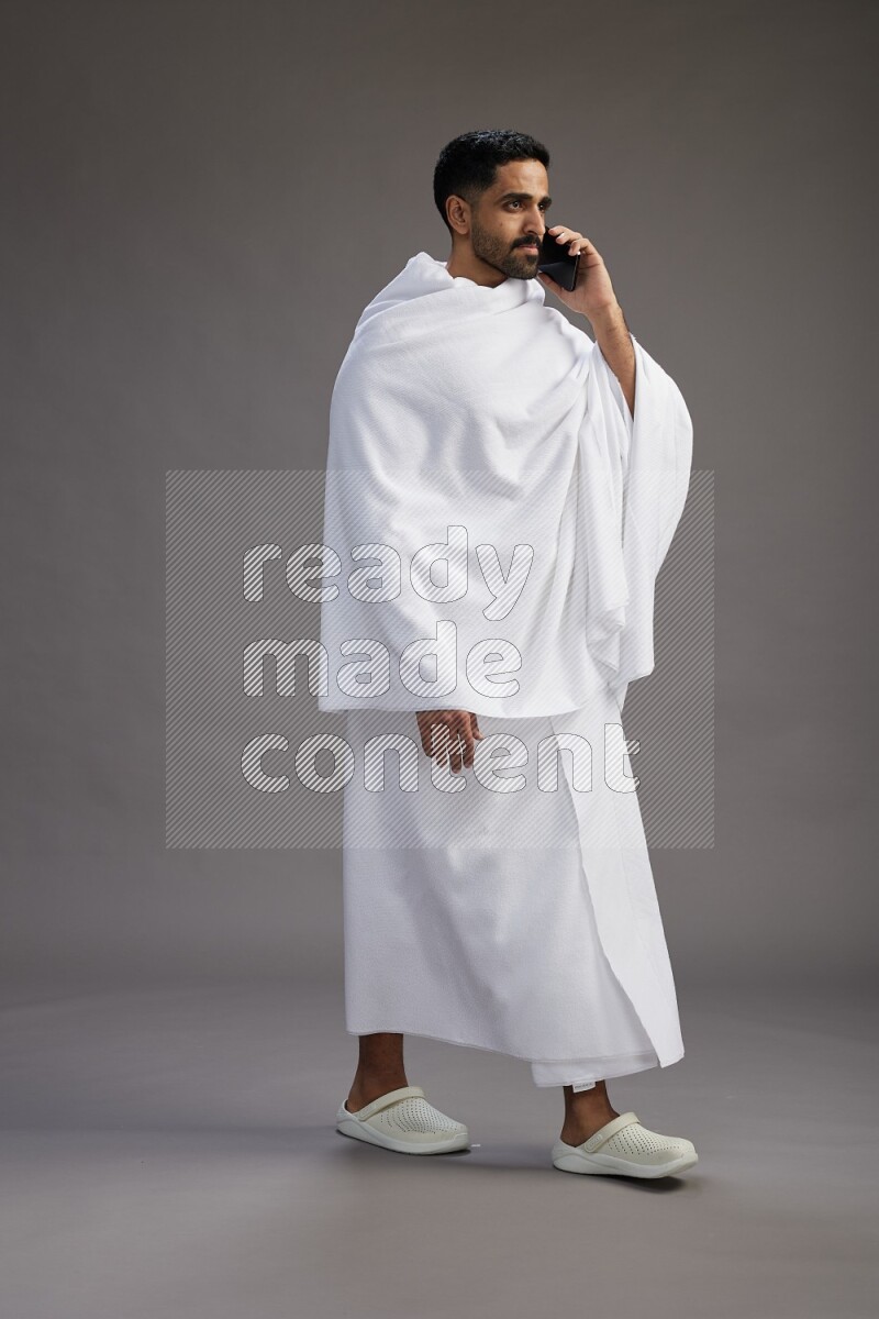 A man wearing Ehram Standing talking on phone on gray background