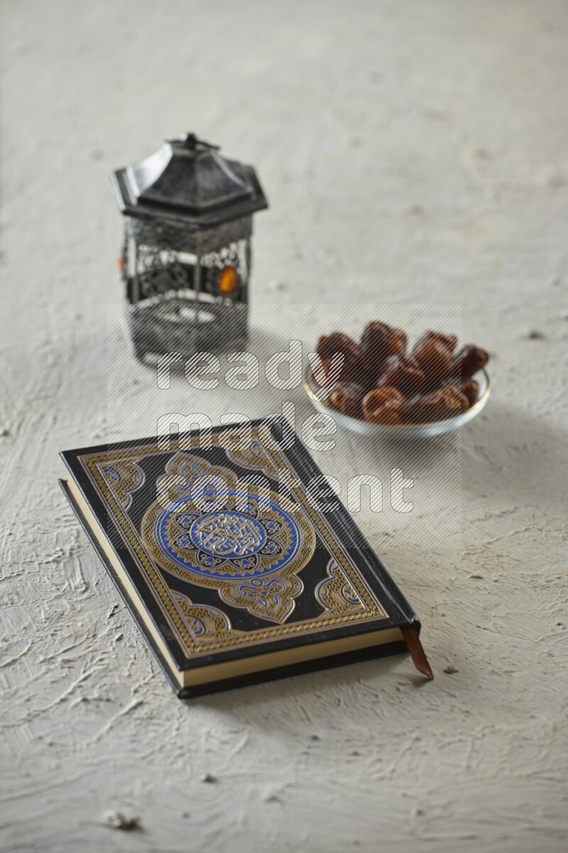 A silver lantern with different drinks, dates, nuts, prayer beads and quran on textured white background
