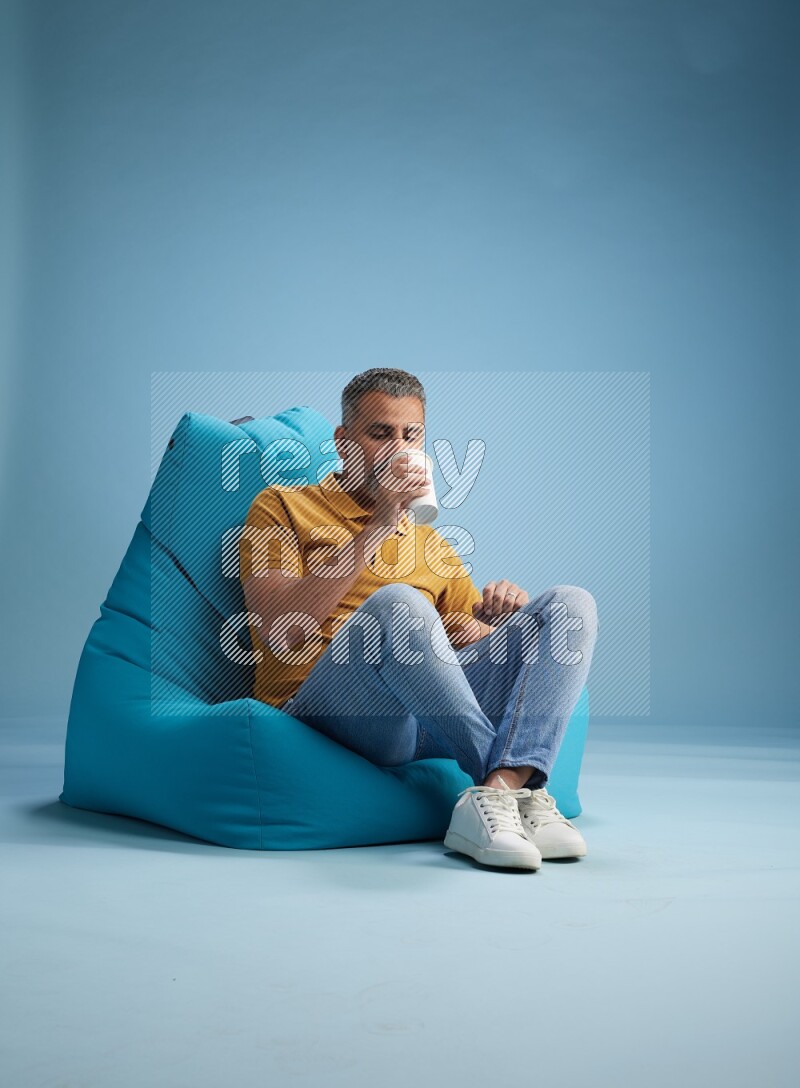 A man sitting on a blue beanbag and drinking coffee