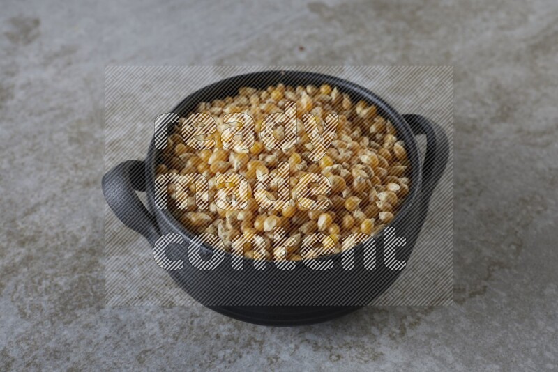 corn kernel in a black handheld ceramic bowl on a grey textured countertop