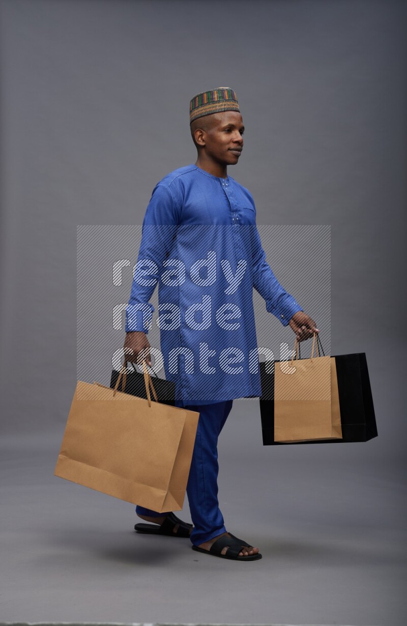 Man wearing Nigerian outfit standing holding shopping bag on gray background