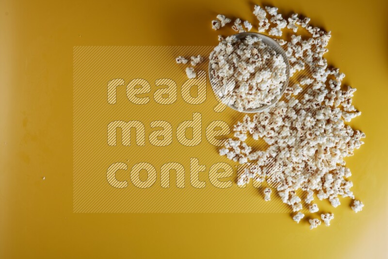 A white pottery bowl full of popcorn with popcorn beside it on a yellow background in different angles