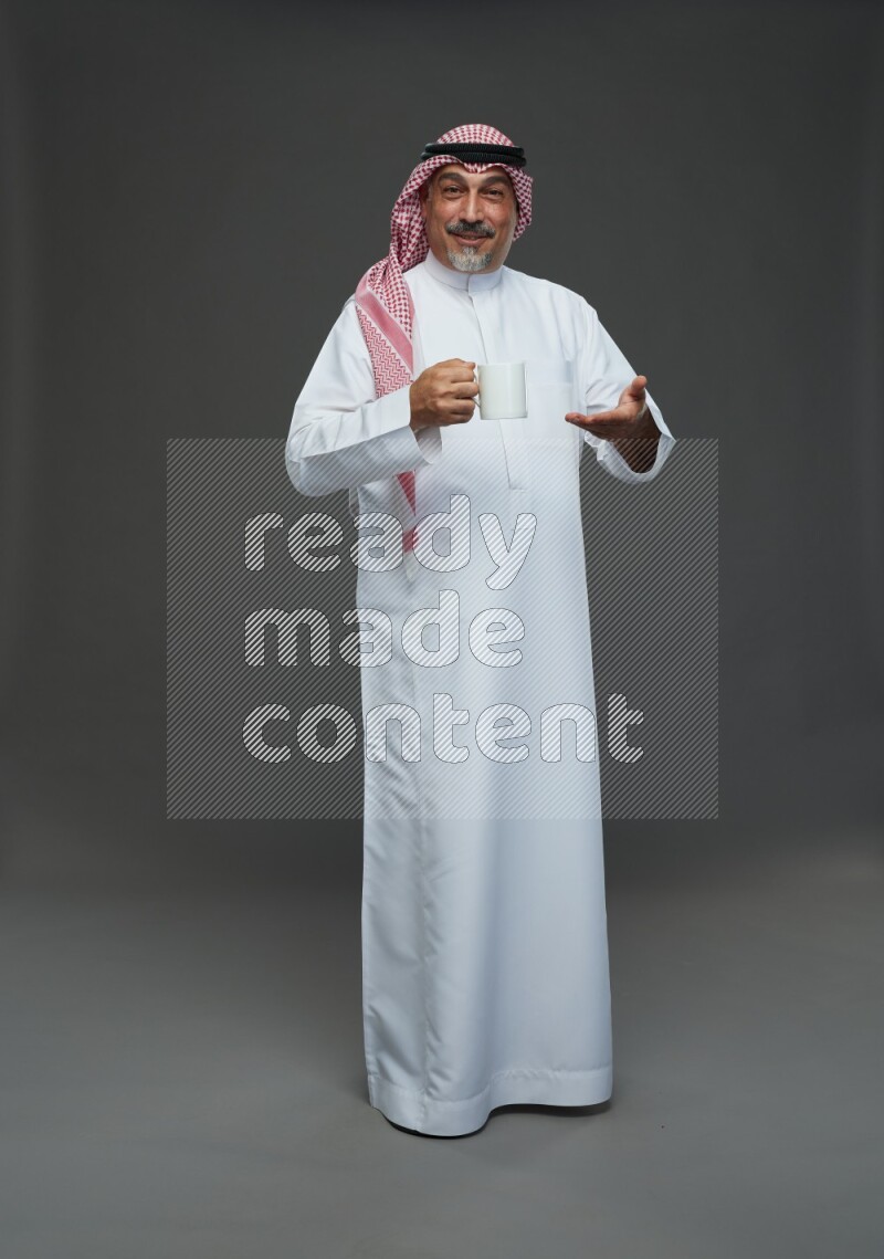 Saudi man with shomag Standing holding mug on gray background