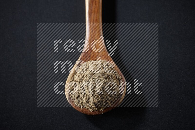 A wooden ladle full of cardamom powder on black flooring