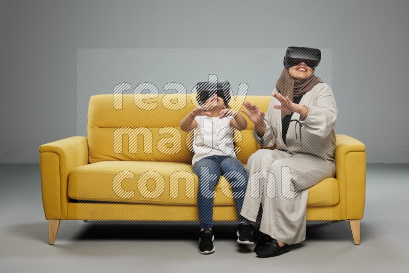 A girl and her mother sitting playing with VR on gray background