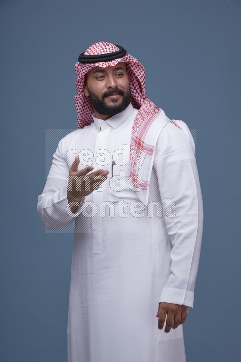 A Saudi man posing on blue background wearing Thob and Shomag