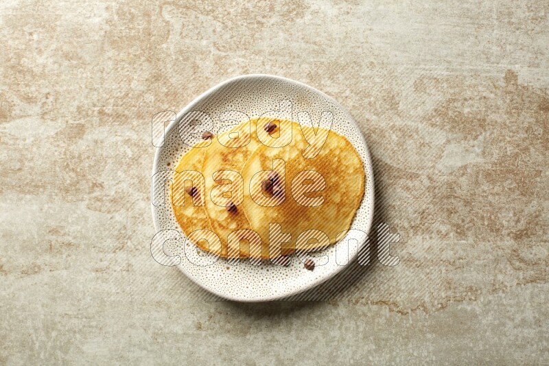 Three stacked chocolate chips pancakes in an irregular plate on beige background