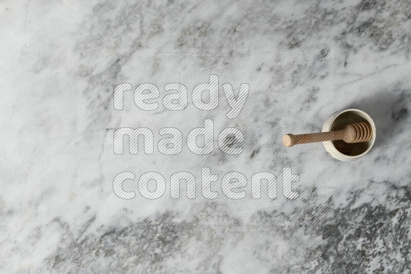 وعاء فخاري أسود مع ملعقة عسل خشبية بداخله على خلفية من الرخام الرمادي