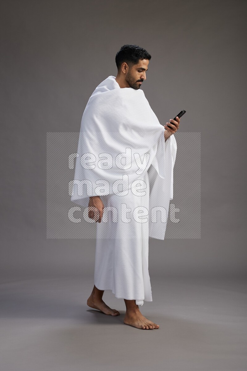 A man wearing Ehram Standing texting on phone on gray background