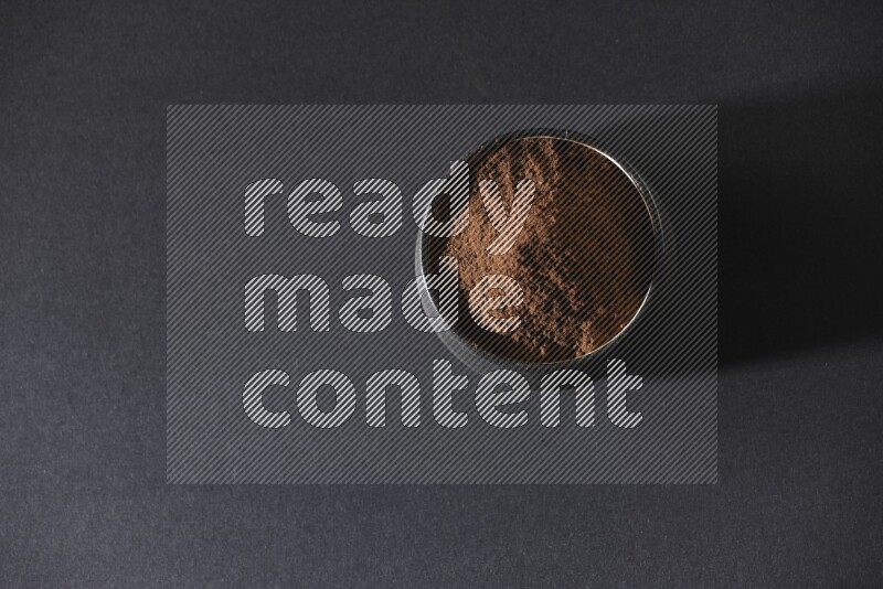 A black pottery bowl full of cloves powder on a black flooring