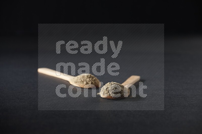 ملعقتان خشبيتان ممتلئتان ببودرة الهيل على خلفية سوداء