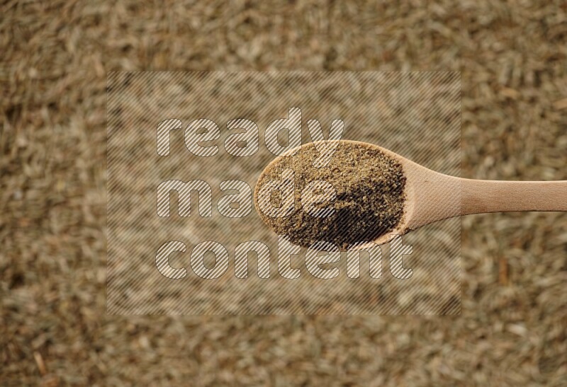 A wooden spoon full of cumin powder on a cumin seeds background