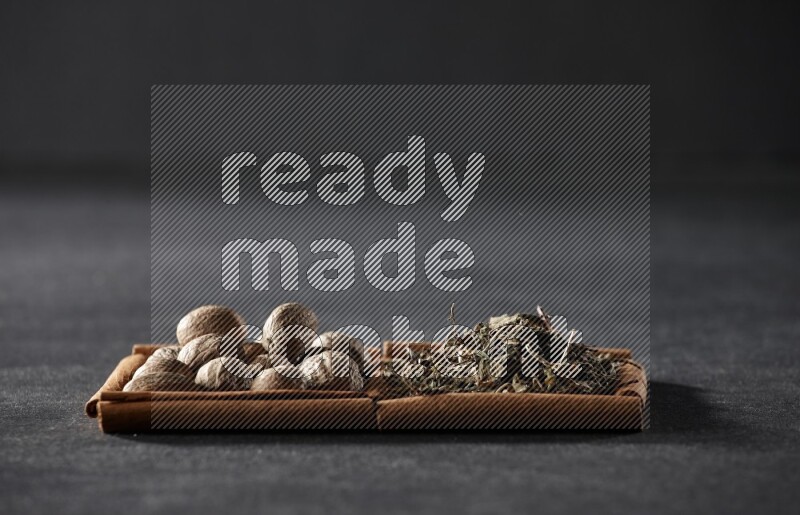 2 squares of cinnamon sticks full of nutmegs and dried basil on black flooring