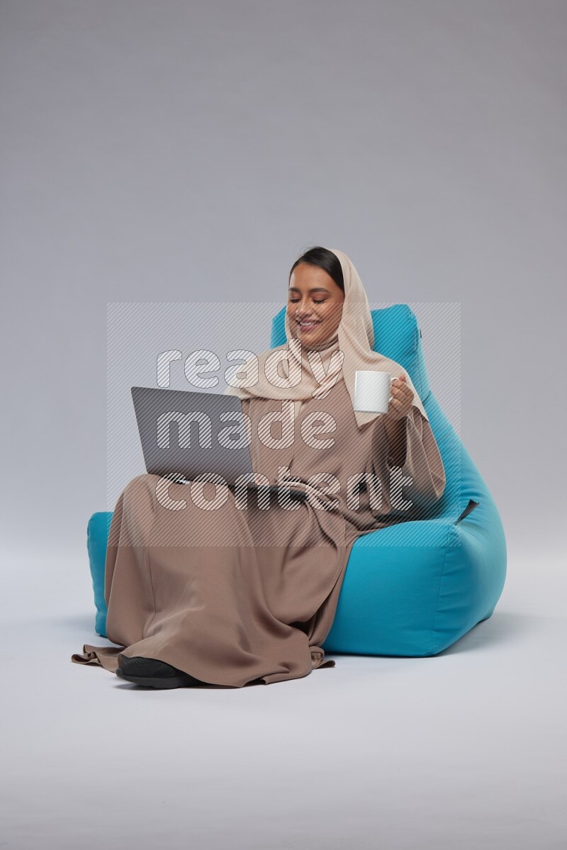 A Saudi woman sitting on a blue beanbag and working on laptop