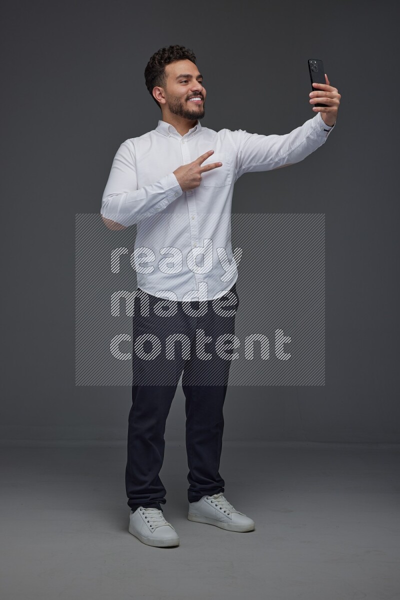 A man wearing smart casual and taking selfie with his phone eye level on a gray background
