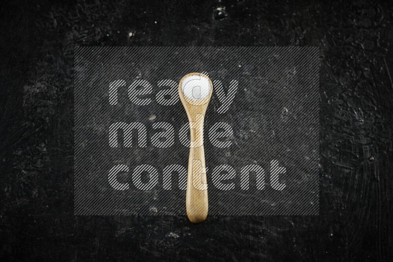A wooden spoon full of white salt on black background