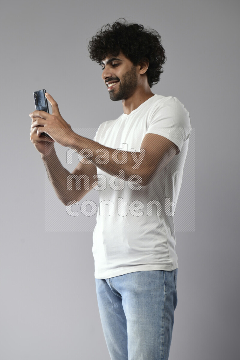 A man wearing casual standing and shooting with his phone on white background