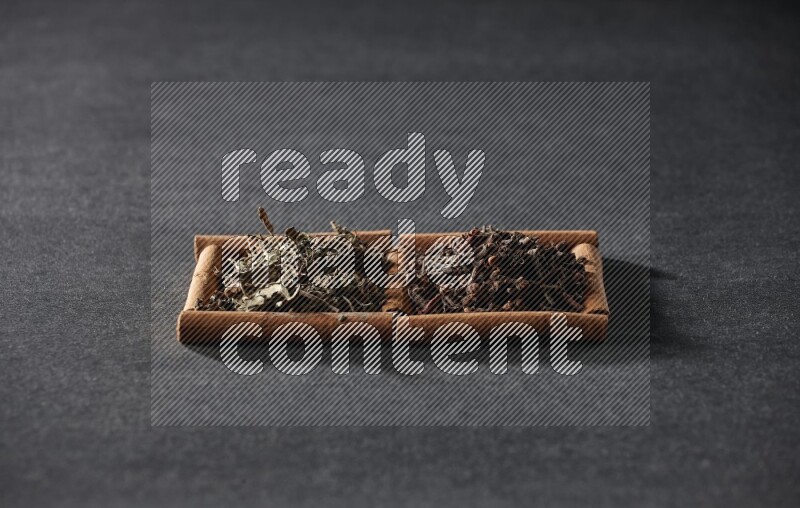 مربعان من أعواد القرفة ممتلئان بالقرنفل والريحان المجفف علي خلفية سوداء