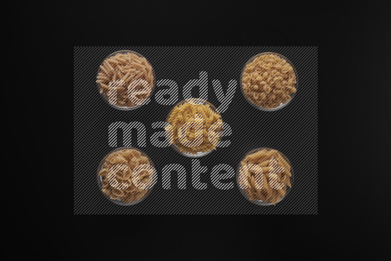 Different pasta types in 5 glass bowls on black background