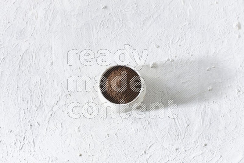 A beige ceramic bowl full of cloves powder on a white flooring