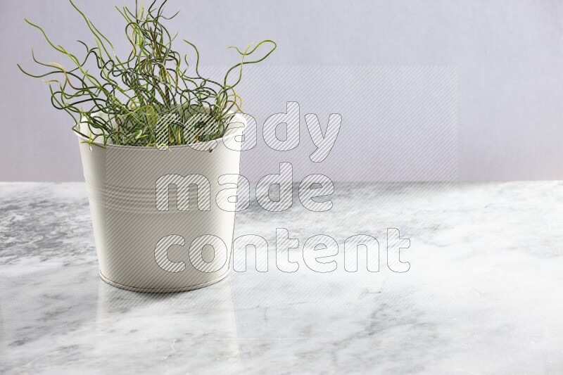 Green artificial plant in white pot on light grey marble background