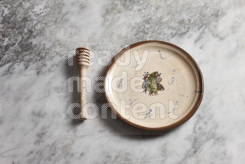 Decorative pottery plate with wooden honey dipper on the side on grey marble background
