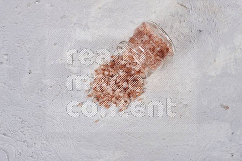 A glass jar full of coarse himalayan salt crystals on white background