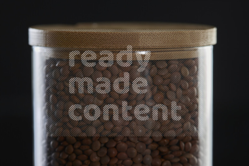 Brown lentils in a glass jar on black background