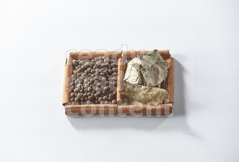 مربعان من أعواد القرفة ممتلئان ببهار الفلفل الحلو وأوراق الغار علي خلفية بيضاء