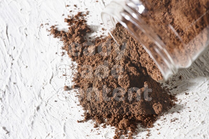 A flipped glass jar full of cloves powder on a textured white flooring