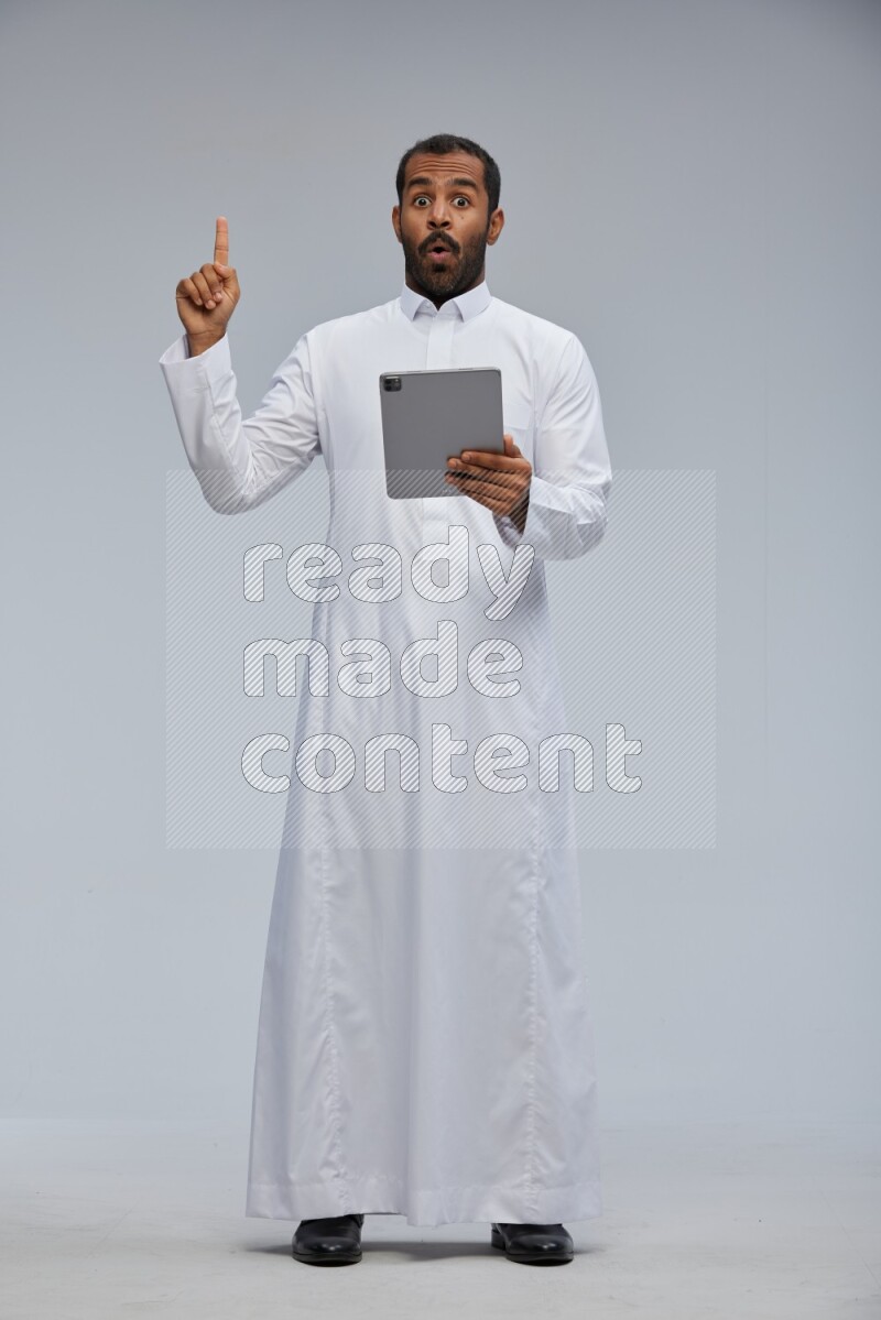 Saudi man wearing Thob standing working on tablet on Gray background