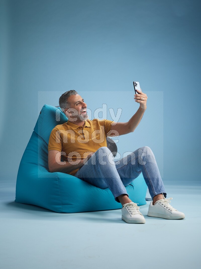 A man sitting on a blue beanbag and taking selfie