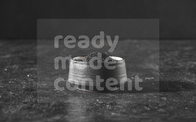 A black pottery bowl full of black seeds on a textured black flooring