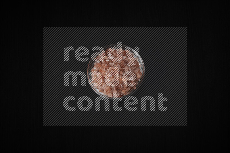 A glass bowl full of coarse himalayan salt crystals on black background